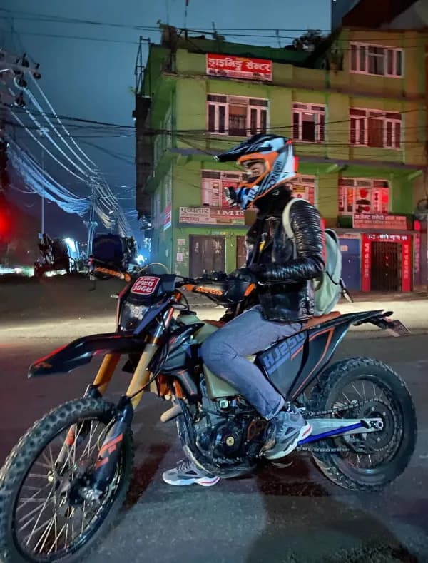 Helmeted rider on a dirt bike at night in a city street